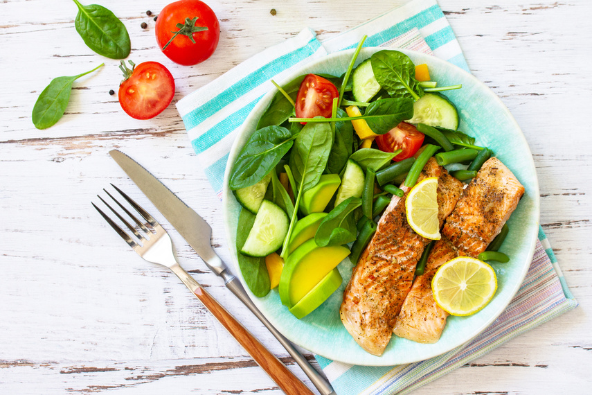 Grilled salmon fillet with spinach, cucumber, tomato and avocado salad on a white wooden table. Top view, flat lay. Copy space.